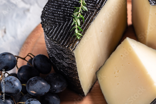 Spanish manchego cheese sliced on a wooden background with rosemary and dark blue grapes. traditional spanish cheese