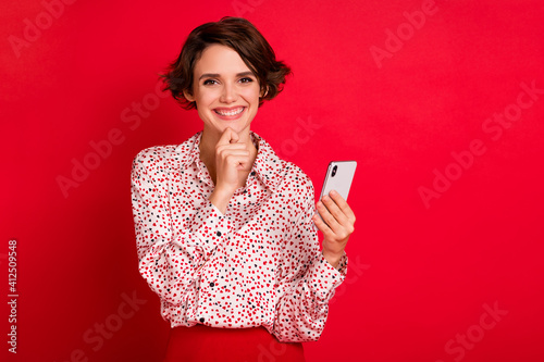 Portrait of lovely cheerful brown-haired girl holding in hands using device gadget 5g isolated over bright red color background