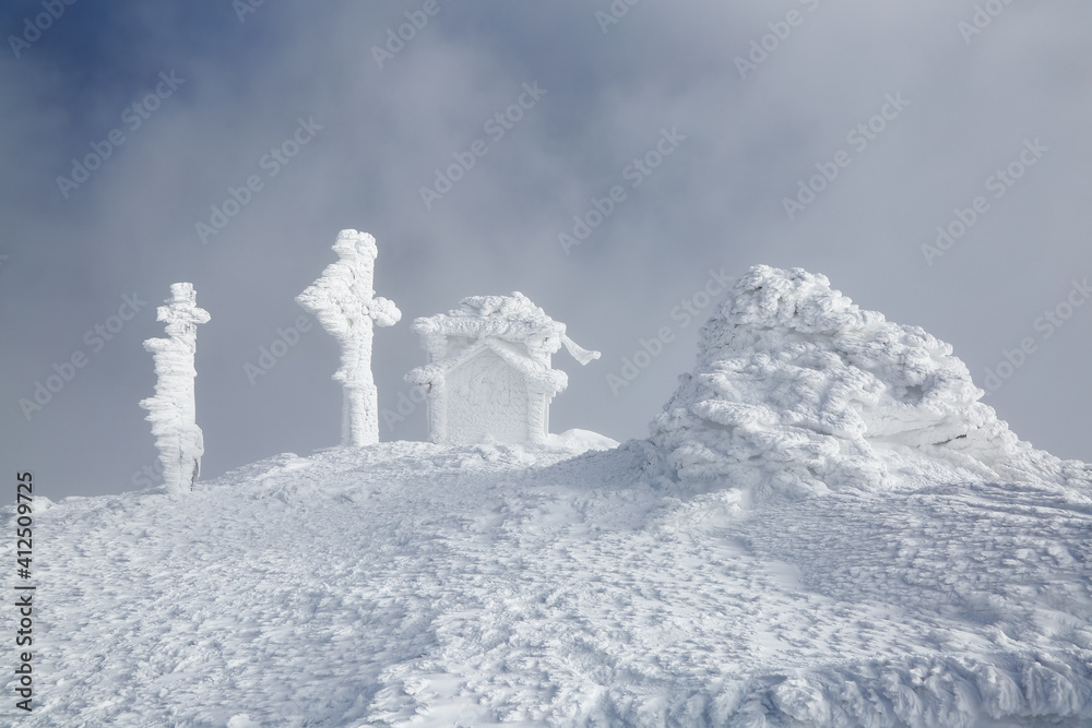 Landscape of high mountains. Snow coted building and cross on a snow covered lawn. Fog on the background. Natural scenery. Location place Carpathian, Ukraine, Europe.