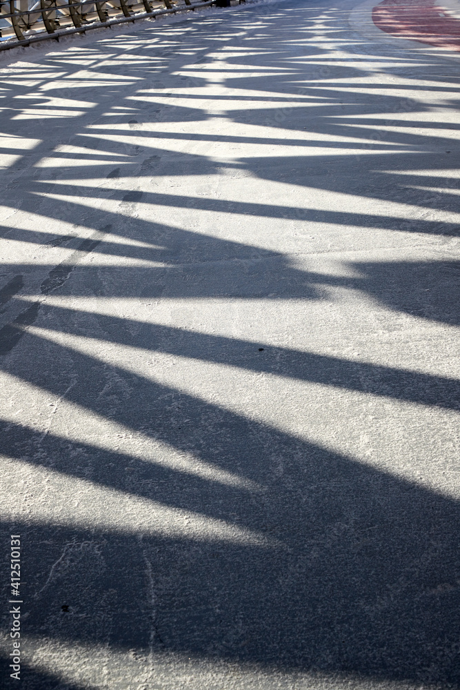 vertical view of geometric shadows of a metal frame on icy pathway of pedestrian bridge