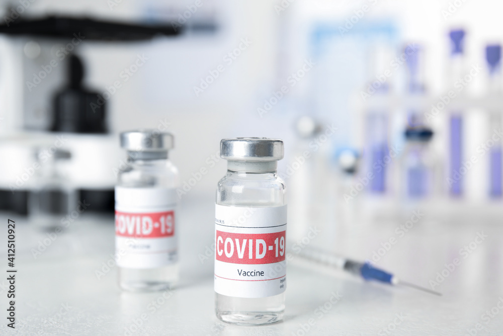 Vials with vaccine against Covid-19 and syringe on white table indoors Vials with vaccine against Covid-19 and syringe on white table indoors