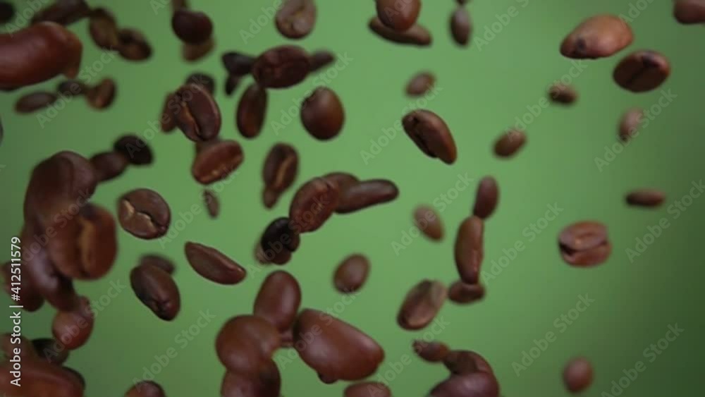 Close-up of roasted arabica coffee beans falling down diagonally on the olive green background in slow motion