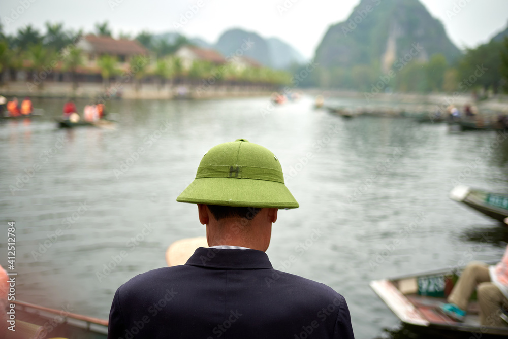 Rear view of Vietnamese man in typical war helmet with scenery of mountains and river.