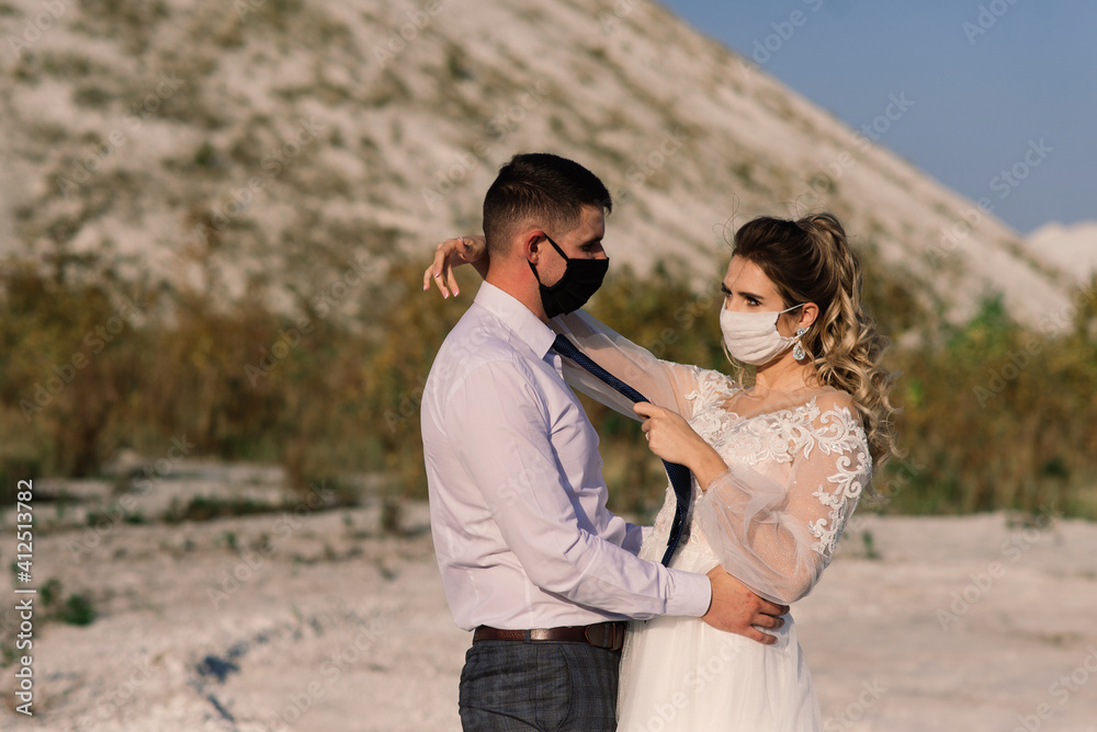 Young loving couple in medical masks in park during quarantine on wedding day. Young loving couple in medical masks in park during quarantine on wedding day.
