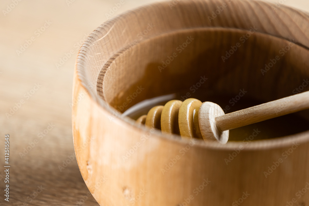 honey in a deep wooden bowl, rustic wooden plate. The wooden spoon drips slowly. honey in a deep wooden bowl, rustic wooden plate. The wooden spoon drips slowly.
