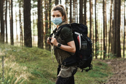 Woman hiker with a backpack wearing prevention mask during her hike in forest