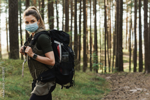 Woman hiker with a backpack wearing prevention mask during her hike in forest