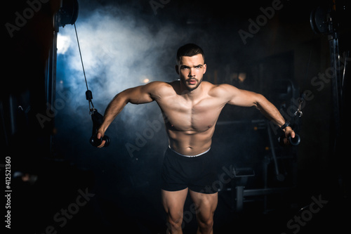 Young sportsman doing pectoral muscle exercise in the gym. Atmosphere smoke