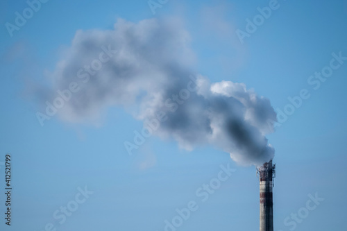 Dirty smoke comes out of the factory chimney polluting the blue clear sky. The concept of the problem of nature pollution, environmental problems.