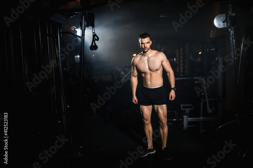 Muscular athlete posing in a dark gym, portrait of a sporty man