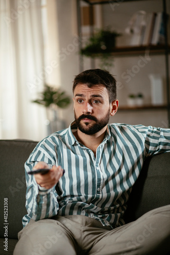 Young man at home. Man sitting in living room watching movie and drinking beer.