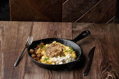 Banosh - a traditional dish in the Western Ukraine made of cornmeal. Served in a black pan with cracklings, mushrooms and hutsul cheese bryndza. Close-up isolated on a wooden background with cutlery.