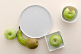 Top view of empty plate, bowls and green fresh pear and apples on the bright table.Space for recipe, text