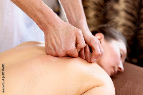 Male massage therapist does back massage to young woman in spa room