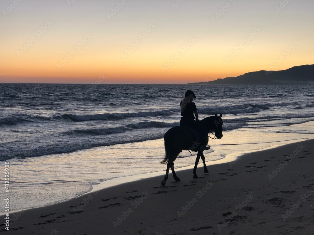 Mujer montando a caballo en la orilla de la playa de Tarifa al atardecer Mujer montando a caballo en la orilla de la playa de Tarifa al atardecer
