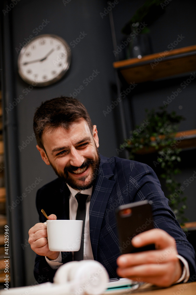 Young businessman using phone and drinking coffee in his office. Handsome man on coffee break. Young businessman using phone and drinking coffee in his office. Handsome man on coffee break.