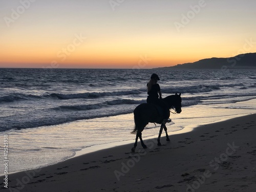 Mujer montando a caballo en la orilla de la playa de Tarifa al atardecer