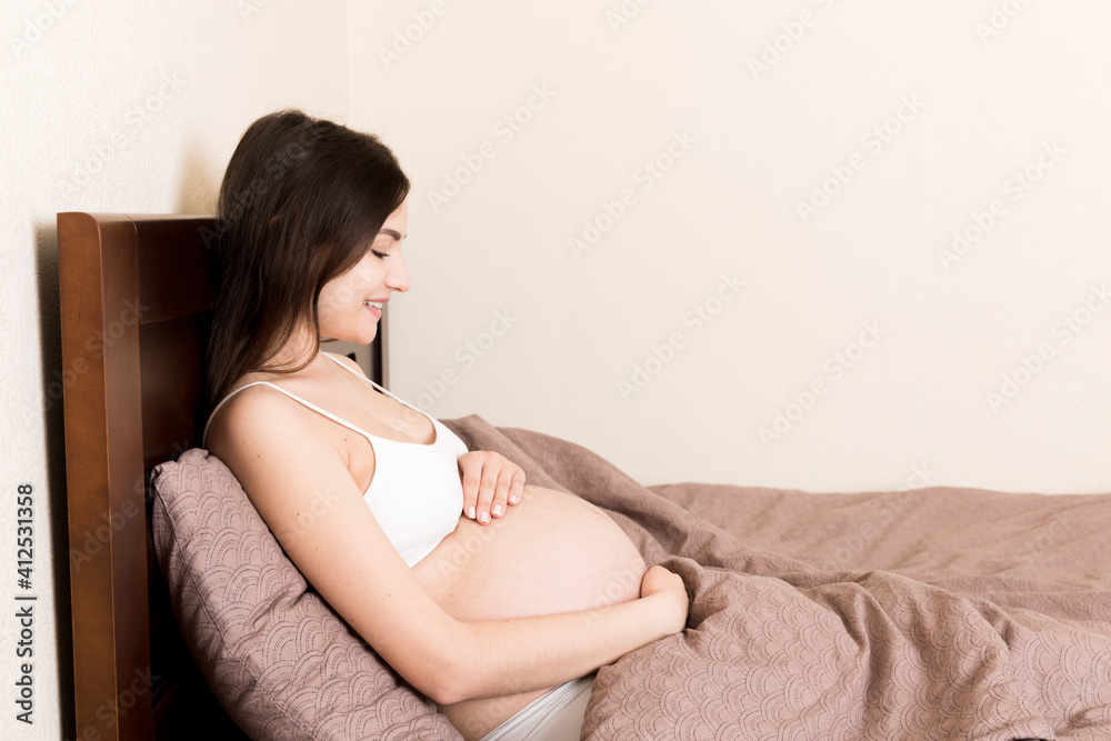 pregnant woman sitting in bed and touching her belly at home. pregnancy expectation concept
