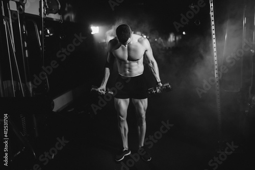 Man an athlete is engaged in a gym, doing an exercise on the muscles of the arms biceps black and white photo