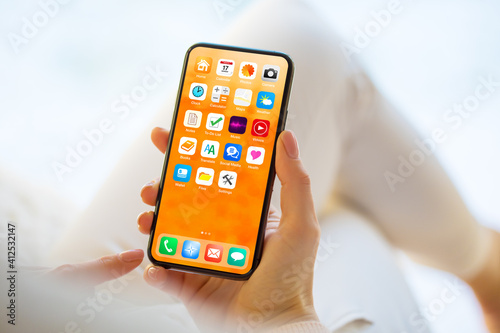 Woman using mobile phone with home screen opened showing different everyday app icons