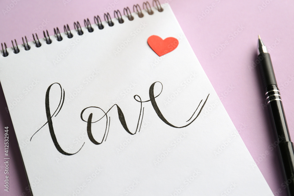 Notebook with handwritten word Love, red paper heart and pen on violet background, closeup