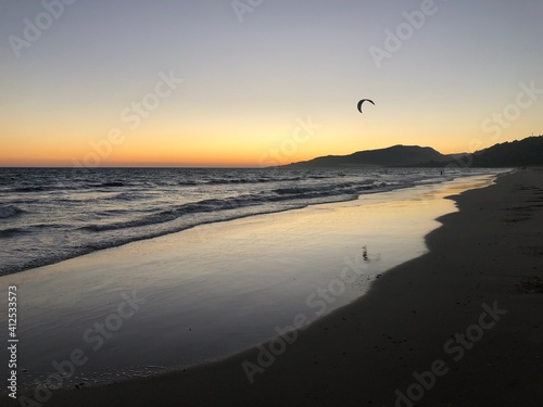 Atardecer con el cielo anaranjado y rosado en la playa cerca del mar en Tarifa con una cometa de kitesurf