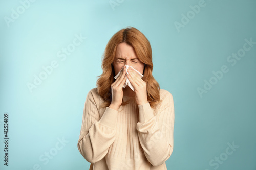 Photos Woman with tissue suffering from runny nose on light blue background