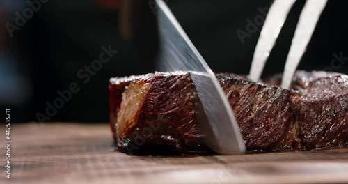 Chef hands cutting meat steak on preparation table, close up. Cook cutting grilled meat on wooden board