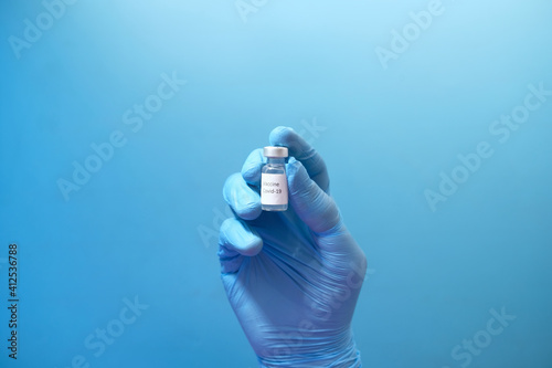 hand in latex gloves holding coronavirus vaccine on blue background 