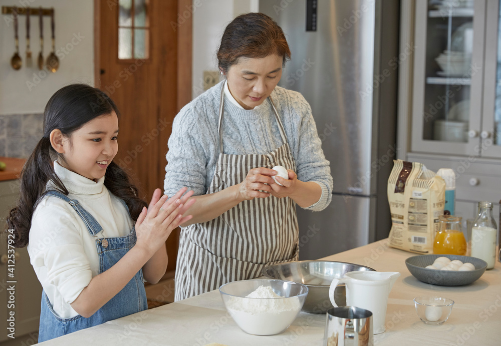 Happy adorable little child girl in apron enjoying cooking homemade pastry together with grandmother at home. Happy adorable little child girl in apron enjoying cooking homemade pastry together with grandmother at home.