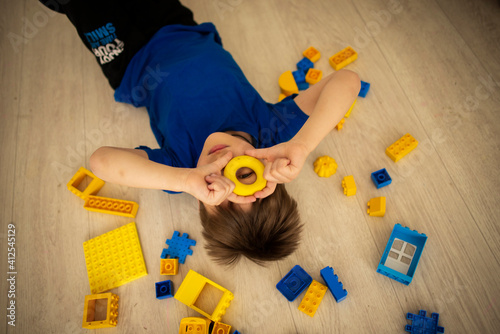 Boy 7-9 years old lying on the floor in the constructor, blue and yellow photo