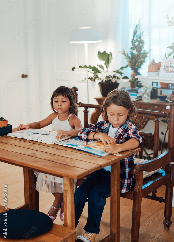 Pretty preschool brother and sister have a good time reading books at table in modern apartment. Pretty preschool brother and sister have a good time reading books at table in modern apartment.