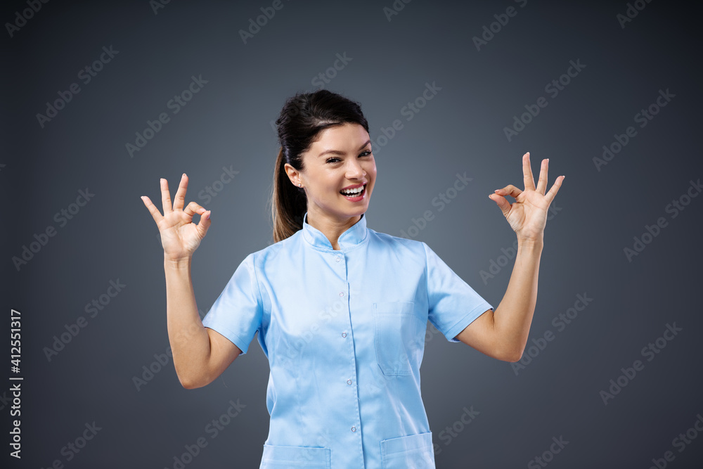 Young smiling female doctor standing and showing okay sign and looking at camera. Young smiling female doctor standing and showing okay sign and looking at camera.