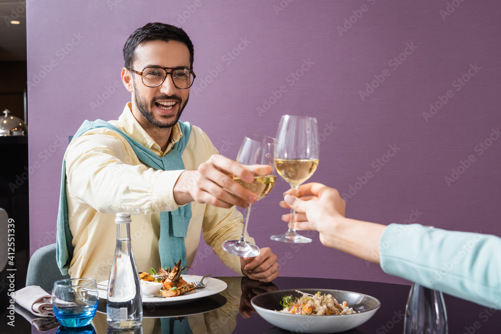 Cheerful arabian man clinking wine with girlfriend near dinner in hotel room Cheerful arabian man clinking wine with girlfriend near dinner in hotel room