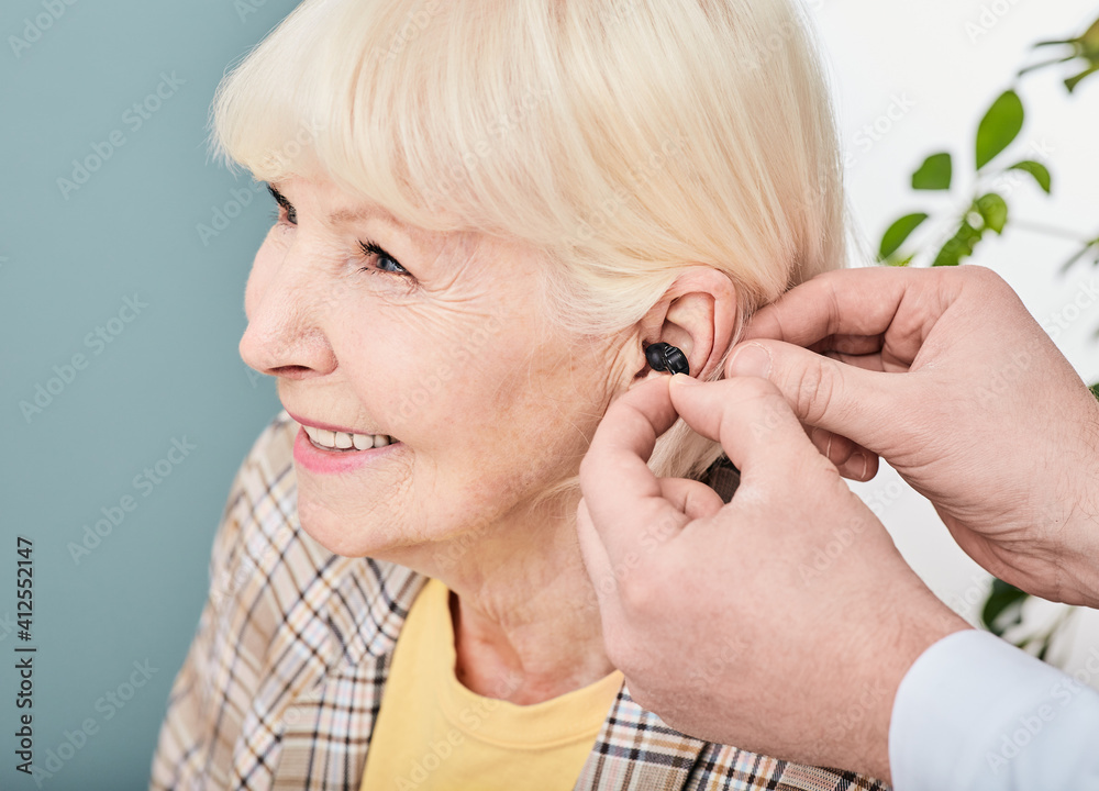 Audiologist inserting Intra-ear hearing aid to senior woman patient, close-up. Hearing solution for elderly people Audiologist inserting Intra-ear hearing aid to senior woman patient, close-up. Hearing solution for elderly people