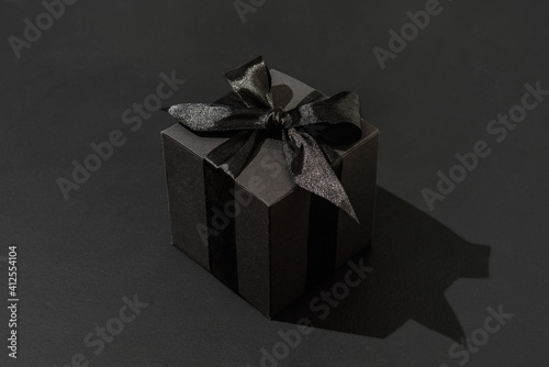 Black gift box with bow on black background. Hard light