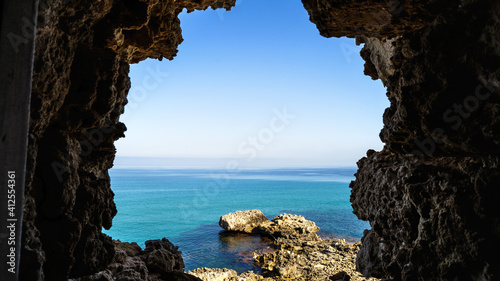 View of blue sea and sky from hole in the rocks. Seascape in rocks window casing frame. Outdoor. Travel tourism. Sicily, Italy