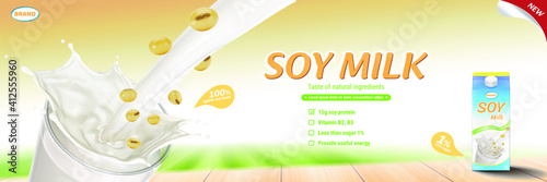 Soy milk pouring down into glass with milk carton and soy beans on wooden table, landscape background