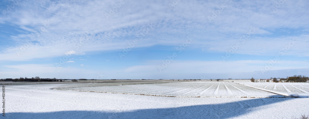 Flat Snow landscape in Tjerkgaast in Friesland, the Netherlands with blue sky, snow and sun. In the front a shadow of an invisible tower. Widescreen photo 