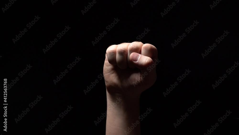 Male Hand of a White Man Clenched into a Fist on a Black Background. Support or Struggle Gesture. Close-Up Male Hand of a White Man Clenched into a Fist on a Black Background. Support or Struggle Gesture. Close-Up