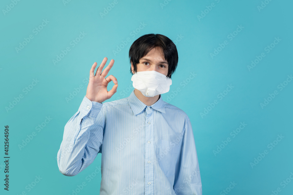 Nice sign. Man in protective face mask isolated on blue studio background. New rules of COVID spreading prevention. Copyspace for ad. Pandemic, healthcare and medicine, coronavirus concept. Flyer Nice sign. Man in protective face mask isolated on blue studio background. New rules of COVID spreading prevention. Copyspace for ad. Pandemic, healthcare and medicine, coronavirus concept. Flyer
