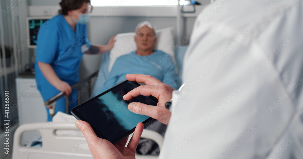 Nurse taking care of aged patient in bed while doctor examining lungs xray on digital tablet Nurse taking care of aged patient in bed while doctor examining lungs xray on digital tablet