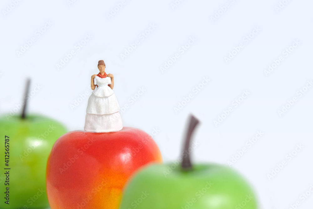 Diet plan before wedding or marriage day concept. Woman standing above apple with trying wedding dress. Miniature people, toys photography. Diet plan before wedding or marriage day concept. Woman standing above apple with trying wedding dress. Miniature people, toys photography.