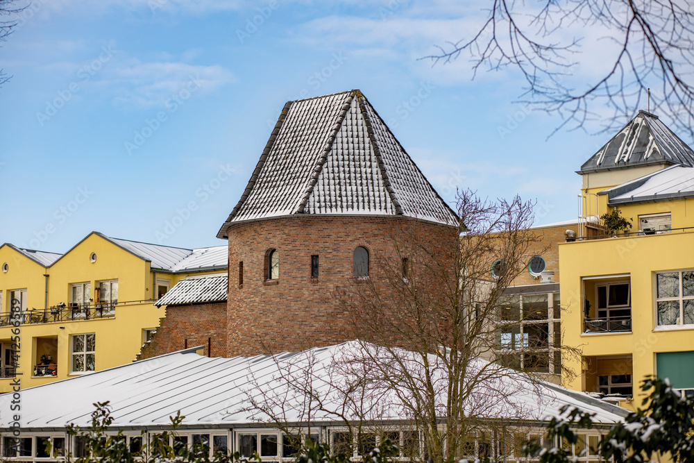 Rooftop of medieval defensive tower among modern yellow painted buildings covered in snow against a blue sky