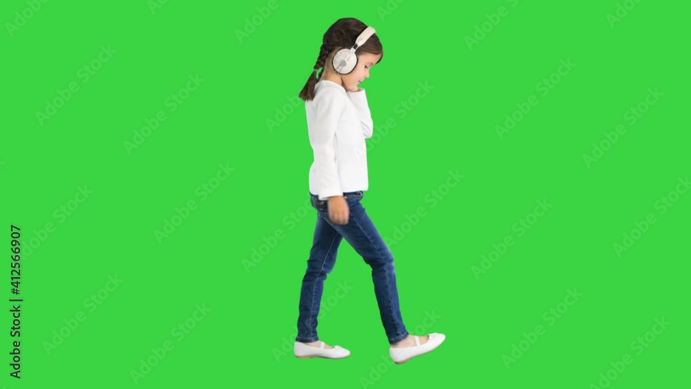 Little girl dressed in white walking in headphones and nodding her head to the music beat on a Green Screen, Chroma Key. Little girl dressed in white walking in headphones and nodding her head to the music beat on a Green Screen, Chroma Key.