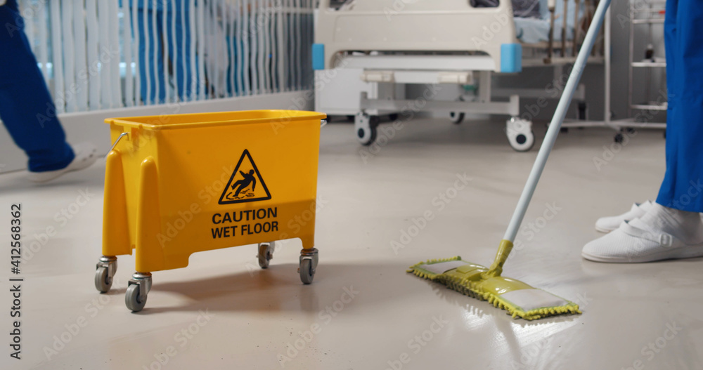 Close up of janitor washing floor with mop and bucket in hospital ward Close up of janitor washing floor with mop and bucket in hospital ward