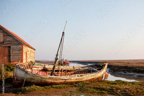 Photography Old barn and boat at Thornham old harbour, Norfolk, England in early morning lig