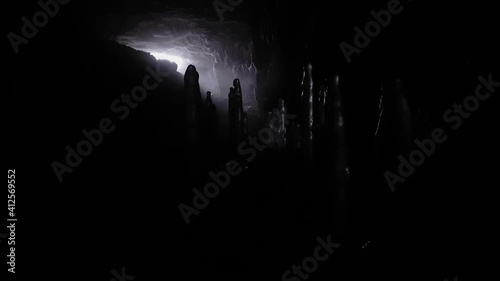 Stalagmites in darkness against the background of exit from cave. Stream of light and steam.