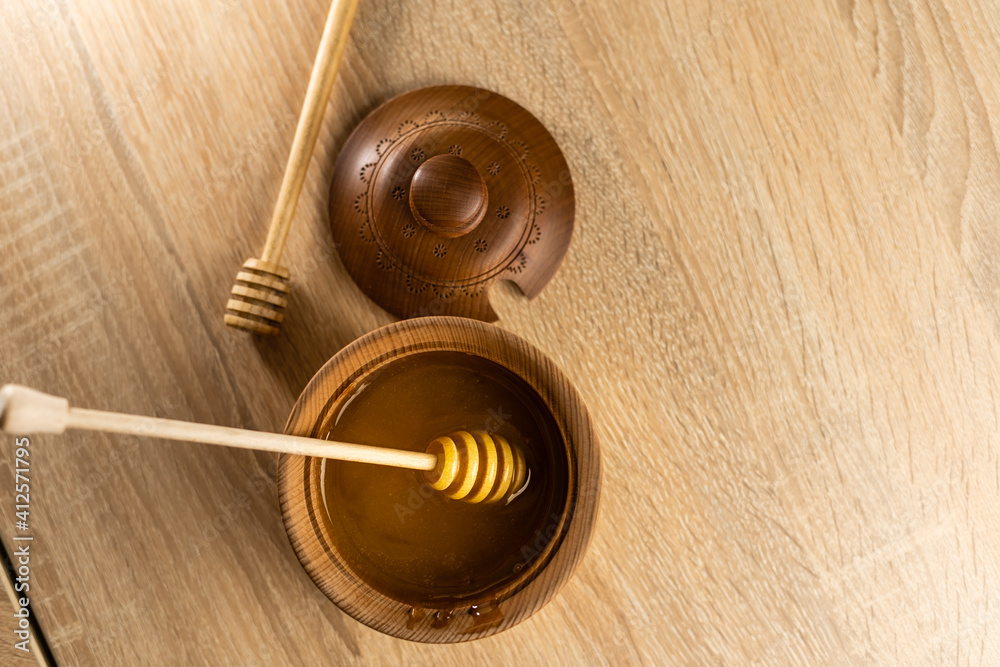 Honey with wooden honey dipper in wooden bowl on wooden table