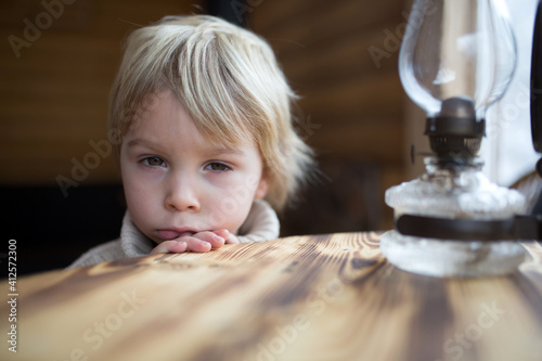 Cute toddler child in a little fancy wooden cottage, reading a book, drinking tea photo